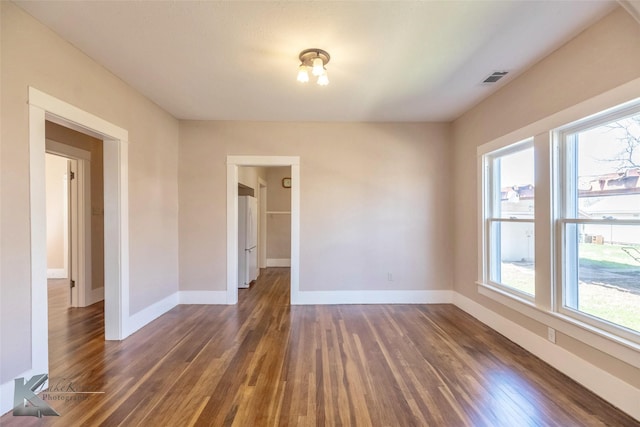 unfurnished room with visible vents, baseboards, and dark wood-style floors