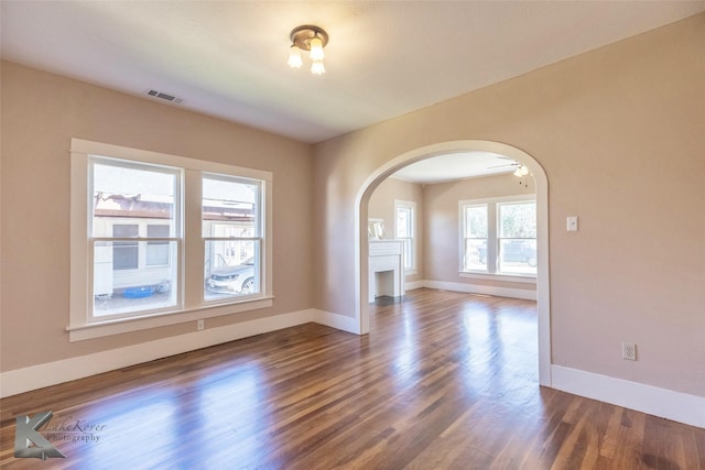 empty room with visible vents, arched walkways, baseboards, and wood finished floors