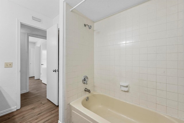 full bath with visible vents, a textured ceiling, wood finished floors, shower / bathing tub combination, and baseboards