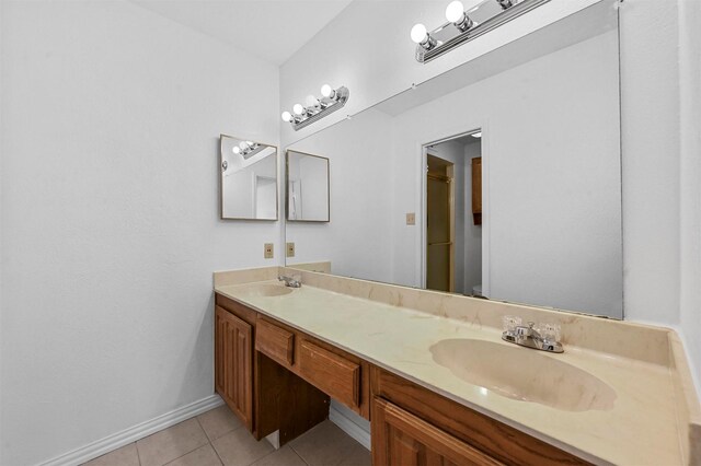 full bathroom with a sink, baseboards, double vanity, and tile patterned flooring