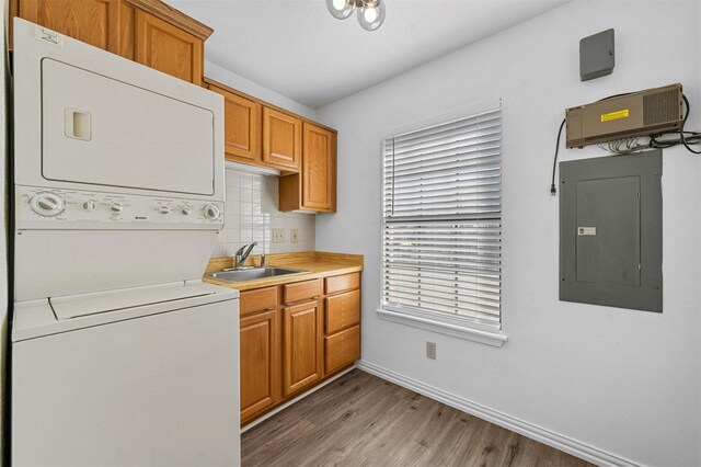 kitchen with light wood-style flooring, electric panel, a sink, stacked washer and clothes dryer, and backsplash