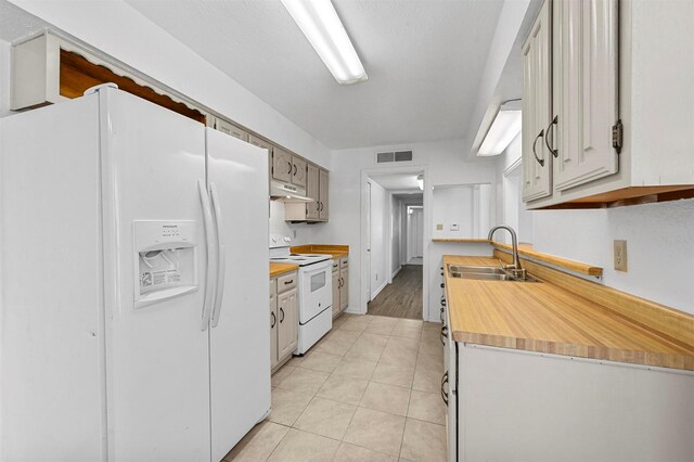 kitchen with visible vents, under cabinet range hood, light tile patterned flooring, white appliances, and a sink