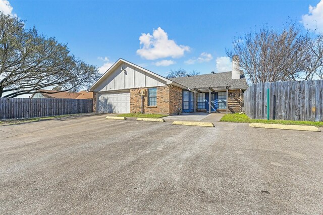 view of front of property with board and batten siding, brick siding, uncovered parking, and fence