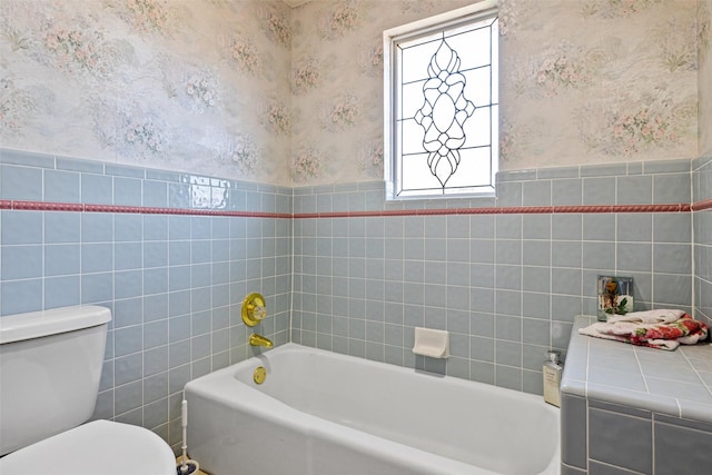 bathroom with a washtub, toilet, wainscoting, and wallpapered walls