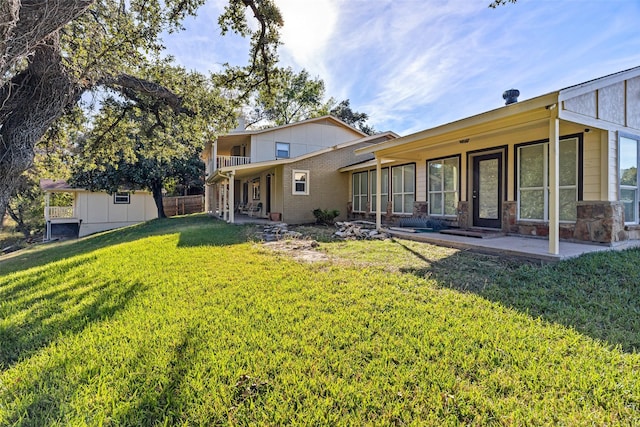 back of house featuring a patio area, stone siding, and a yard