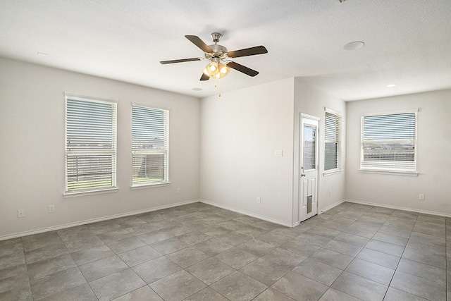 empty room with a wealth of natural light, a ceiling fan, and baseboards