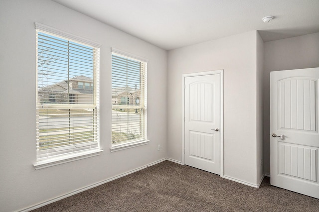 unfurnished bedroom with dark carpet and baseboards