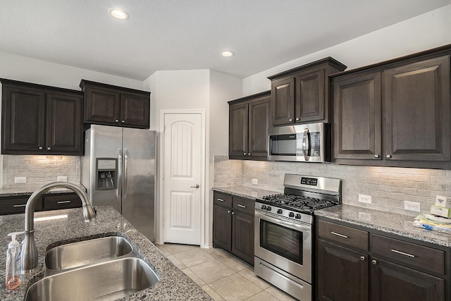 kitchen with stone counters, light tile patterned flooring, a sink, dark brown cabinets, and appliances with stainless steel finishes