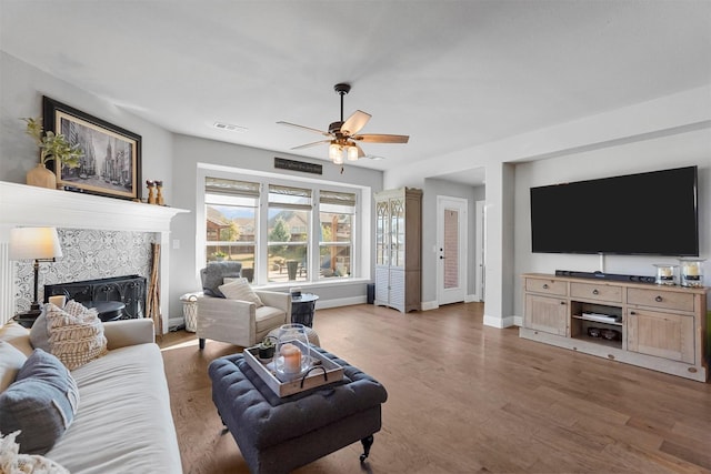 living area featuring a high end fireplace, visible vents, baseboards, wood finished floors, and a ceiling fan