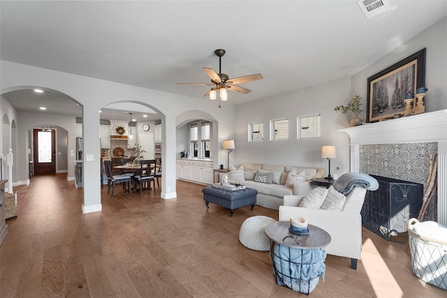 living area with visible vents, a tiled fireplace, wood finished floors, arched walkways, and ceiling fan