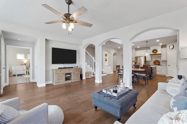 living room featuring stairs, baseboards, light wood-style floors, and a ceiling fan