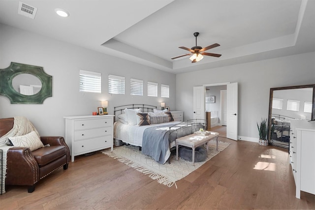 bedroom featuring visible vents, a raised ceiling, baseboards, and wood finished floors