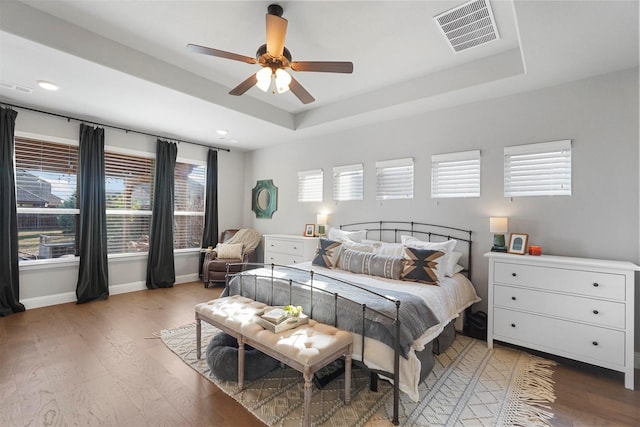 bedroom featuring a tray ceiling, visible vents, light wood-type flooring, and baseboards