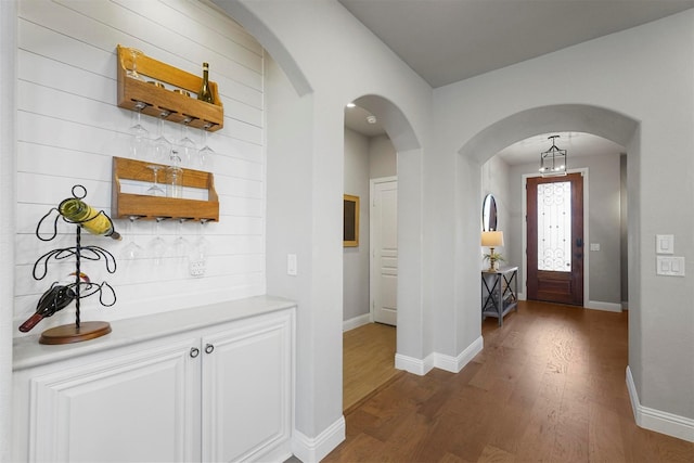 foyer entrance with arched walkways, a dry bar, baseboards, and wood finished floors