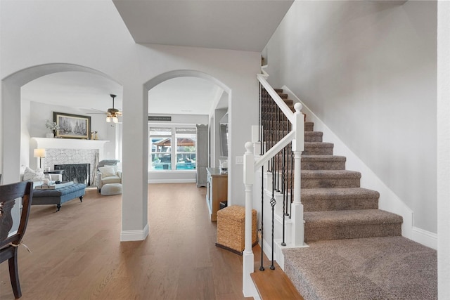 foyer featuring a ceiling fan, wood finished floors, a fireplace, baseboards, and stairs