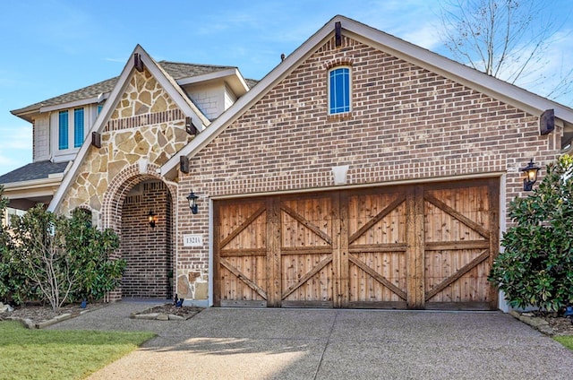 english style home featuring a garage, brick siding, stone siding, and driveway