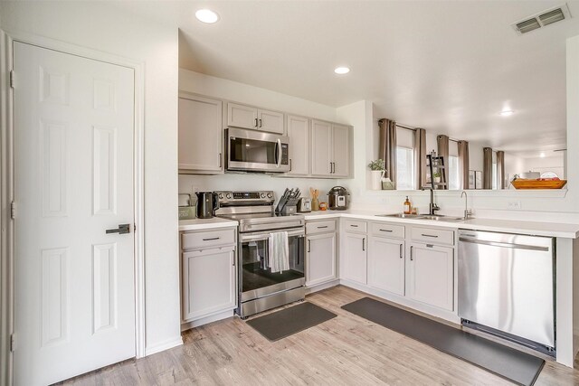 kitchen featuring visible vents, light countertops, light wood-style flooring, stainless steel appliances, and a sink