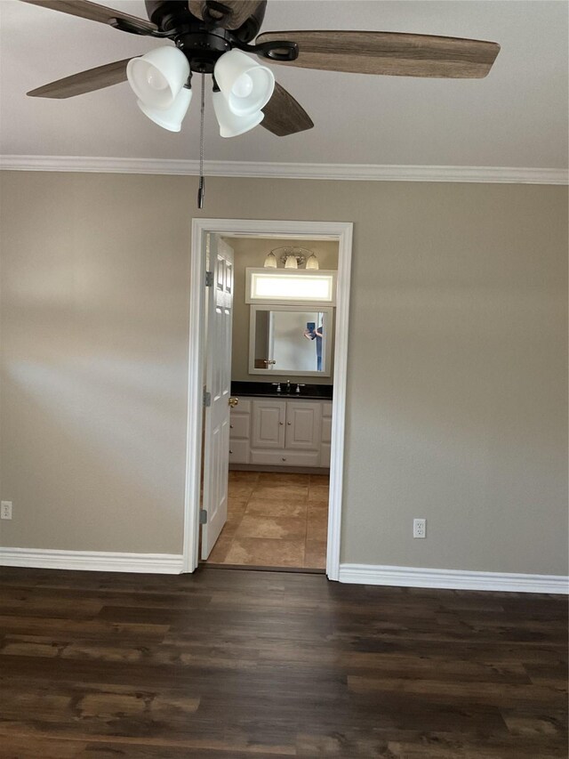 spare room with a sink, baseboards, wood finished floors, and ornamental molding