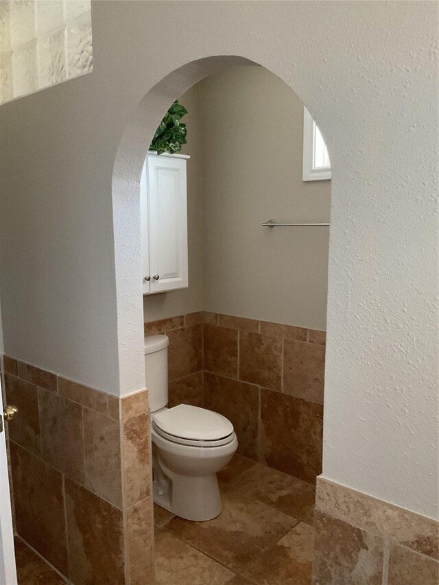 bathroom with tile walls, toilet, and wainscoting