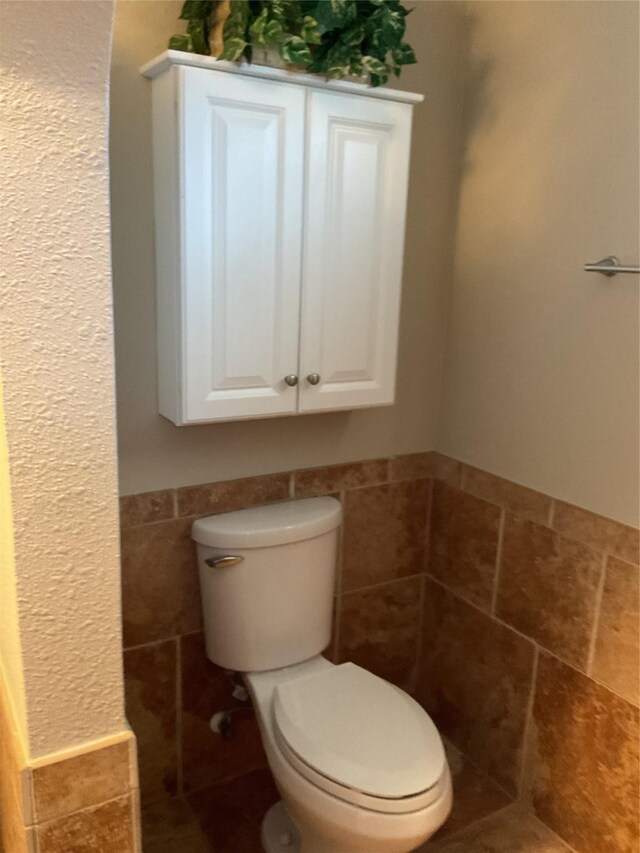 bathroom featuring a wainscoted wall, toilet, and tile walls