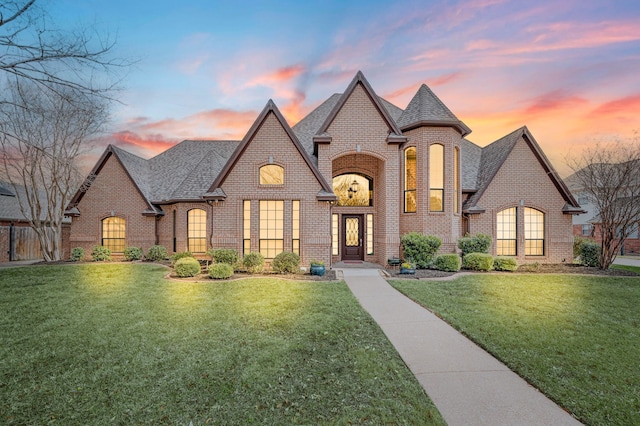 french country inspired facade featuring a lawn, brick siding, and roof with shingles