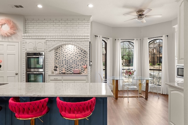 kitchen featuring visible vents, stainless steel double oven, white cabinets, light wood finished floors, and light stone countertops