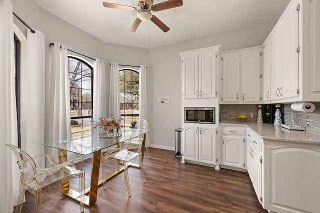 kitchen with dark wood-style floors, ceiling fan, white cabinetry, stainless steel microwave, and tasteful backsplash