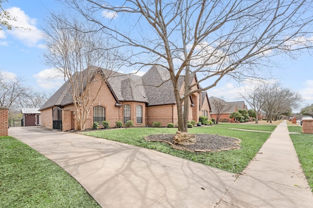 french country inspired facade featuring a front lawn, a garage, brick siding, and a shingled roof