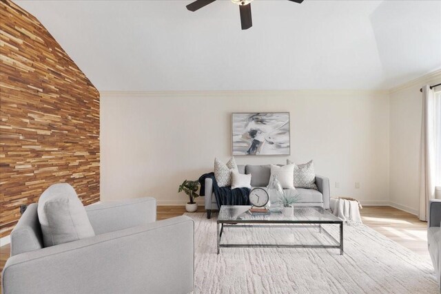 living room featuring baseboards, lofted ceiling, ceiling fan, crown molding, and light wood-type flooring