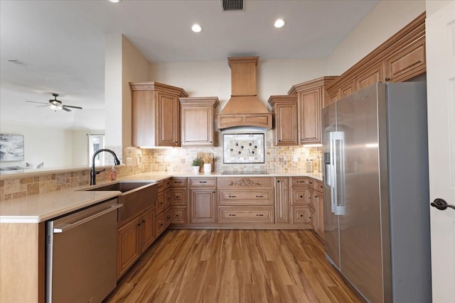 kitchen with light countertops, custom range hood, decorative backsplash, light wood-style flooring, and stainless steel appliances