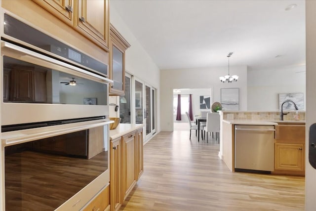 kitchen featuring light wood finished floors, a sink, light countertops, glass insert cabinets, and appliances with stainless steel finishes