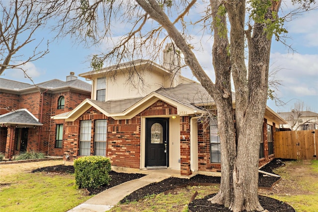 view of front of house featuring fence, brick siding, and roof with shingles