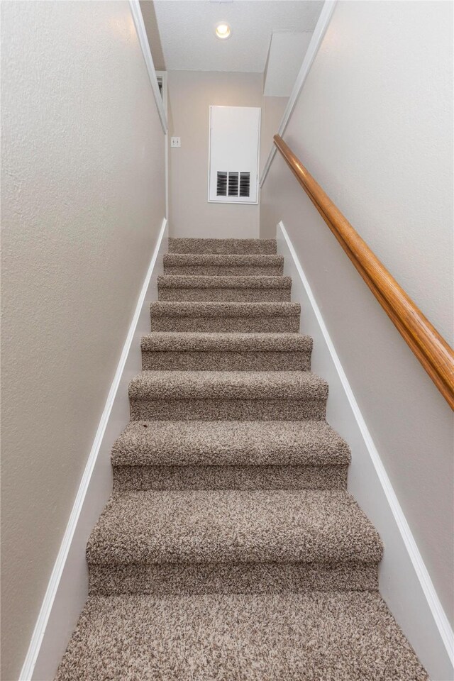 staircase with visible vents, recessed lighting, and a textured wall