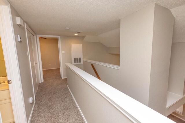 hall with visible vents, an upstairs landing, a textured ceiling, and carpet floors