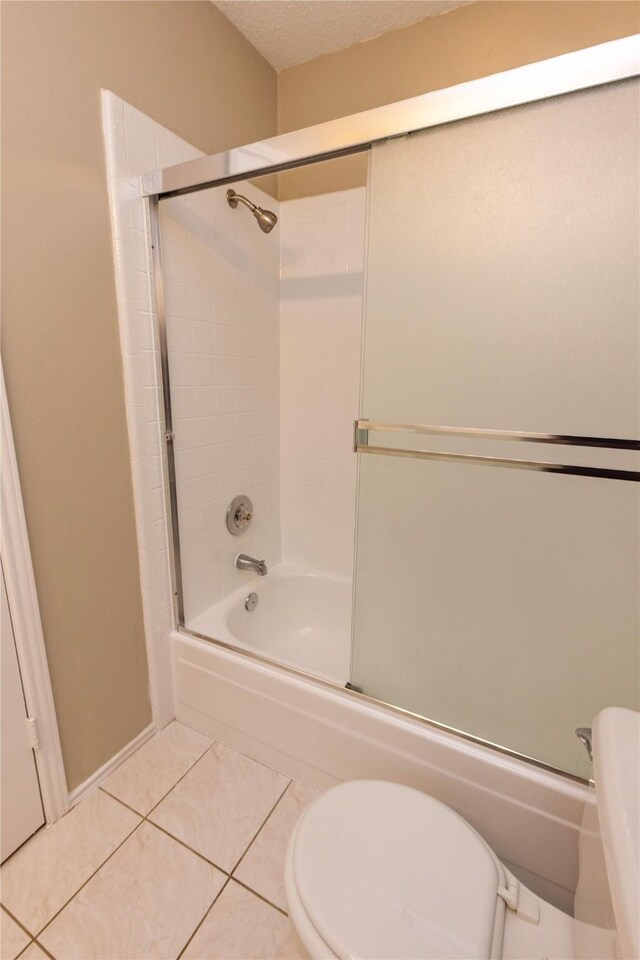 full bathroom with tile patterned flooring, a textured ceiling, toilet, and bath / shower combo with glass door