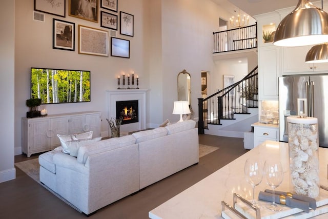 living room featuring stairway, baseboards, visible vents, a high ceiling, and a warm lit fireplace