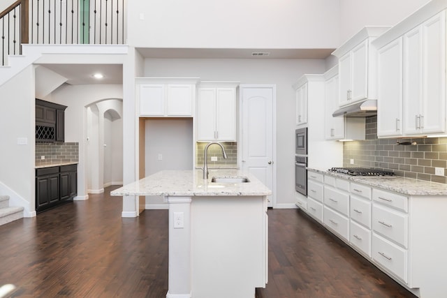 kitchen featuring a sink, under cabinet range hood, white cabinetry, stainless steel appliances, and arched walkways