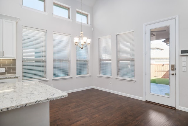 unfurnished dining area featuring dark wood finished floors, a high ceiling, a notable chandelier, and baseboards