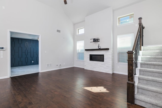 unfurnished living room featuring visible vents, wood-type flooring, a stone fireplace, and ceiling fan