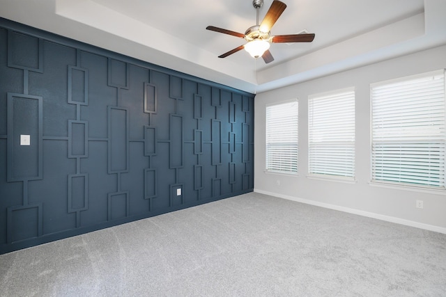 carpeted spare room featuring a tray ceiling, baseboards, a ceiling fan, and a decorative wall