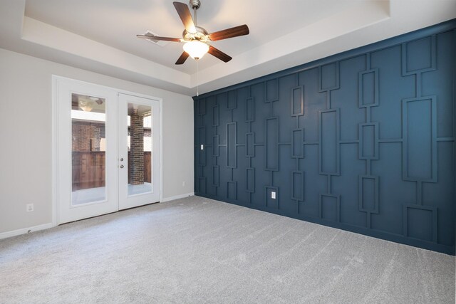 carpeted empty room featuring ceiling fan, baseboards, a tray ceiling, french doors, and a decorative wall