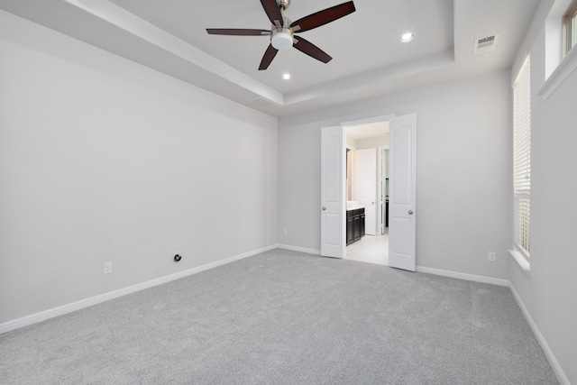 unfurnished bedroom with a tray ceiling, multiple windows, visible vents, and baseboards