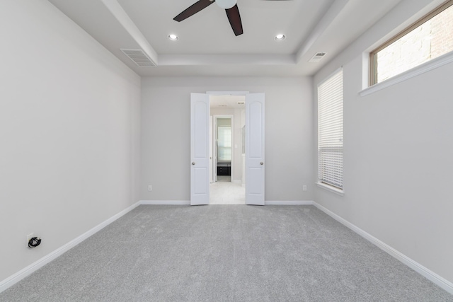 empty room with a tray ceiling, baseboards, visible vents, and carpet floors