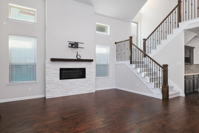 unfurnished living room featuring a fireplace, dark wood-style flooring, a towering ceiling, and baseboards