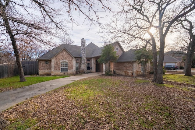 view of front of home with a front yard, fence, driveway, a chimney, and brick siding