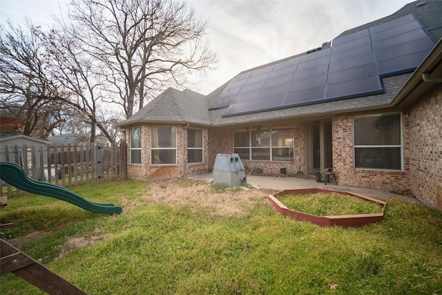 back of house featuring a patio, fence, a shingled roof, brick siding, and solar panels