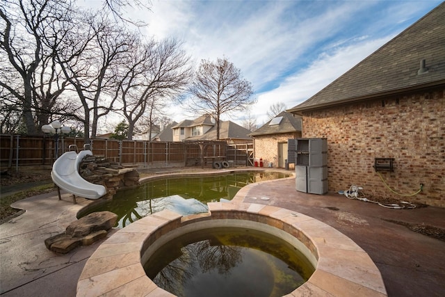 view of swimming pool featuring a patio, a pool with connected hot tub, a fenced backyard, and a water slide