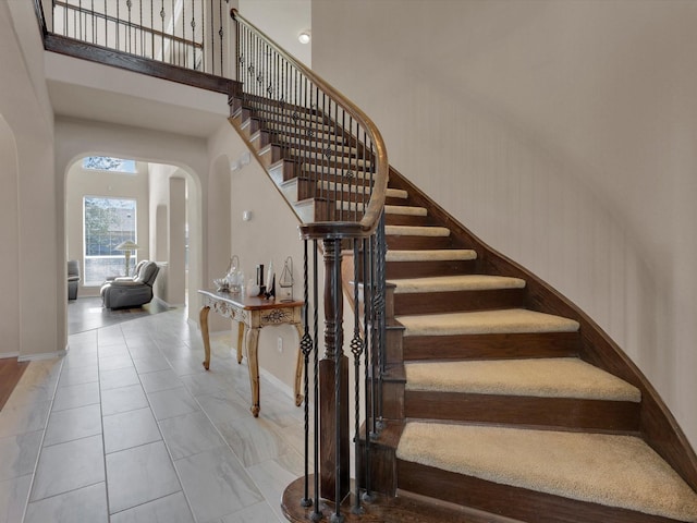 staircase featuring arched walkways, tile patterned flooring, a high ceiling, and baseboards