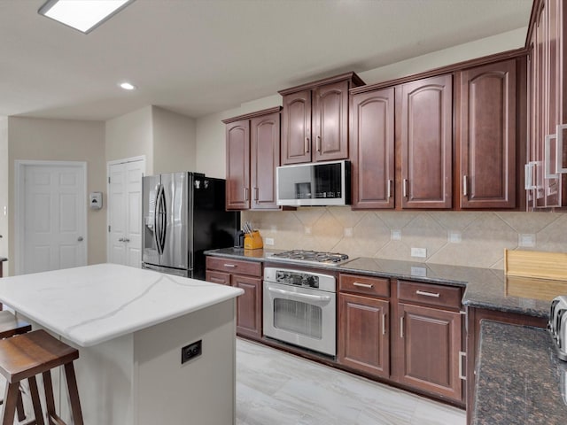 kitchen featuring tasteful backsplash, a center island, a breakfast bar, dark stone counters, and appliances with stainless steel finishes