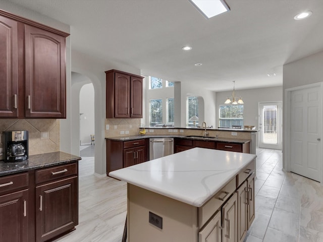 kitchen featuring a sink, a kitchen island, a peninsula, arched walkways, and stainless steel dishwasher